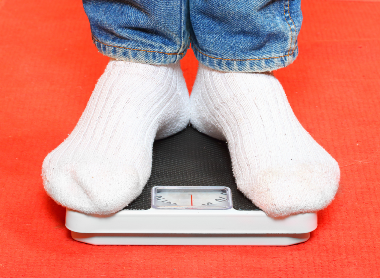 person weighing himself on standing on scale with jeans and white socks with a red background